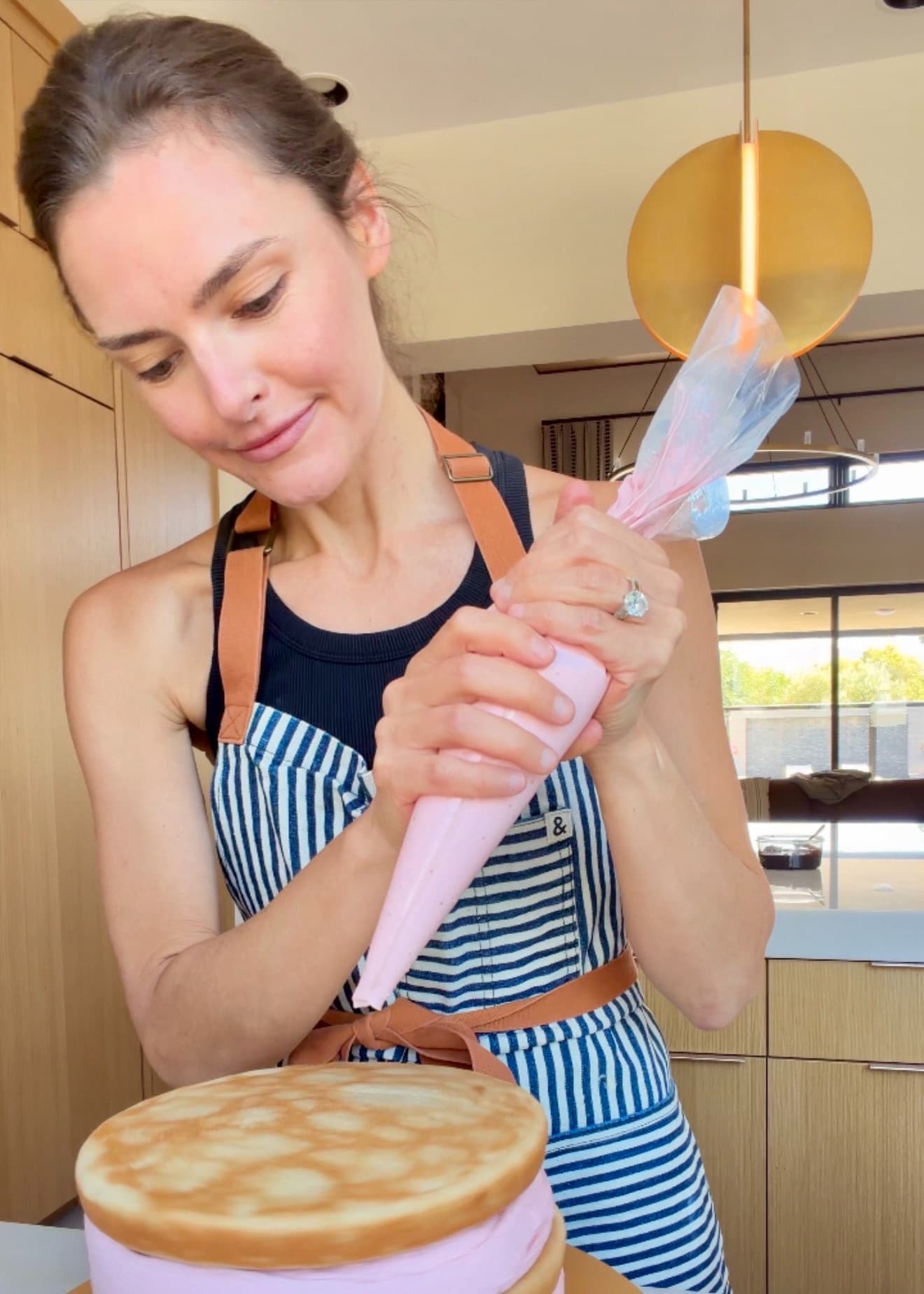 Angela piping pink frosting onto a layer cake in her kitchen