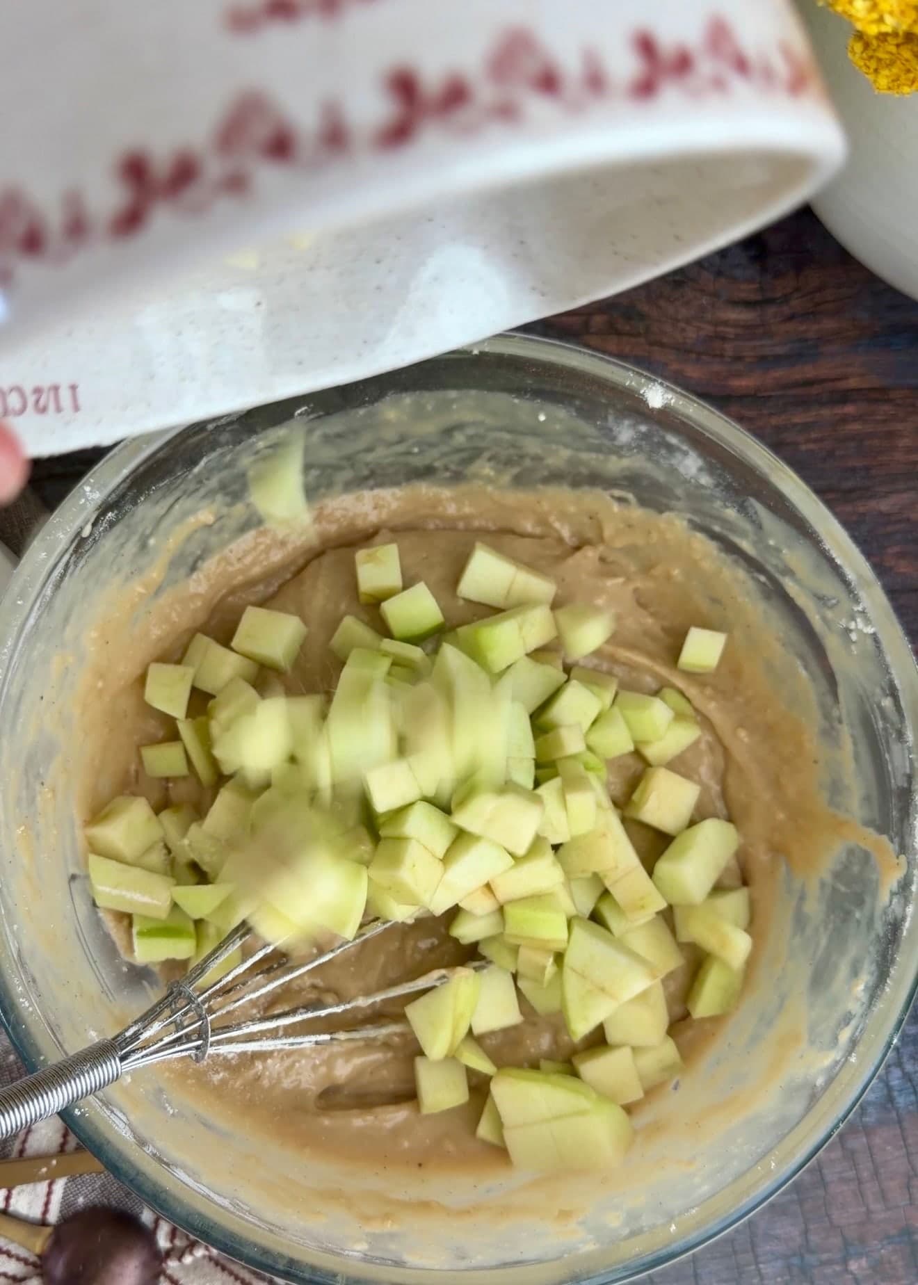 Small apple pieces falling into the bowl of cake batter