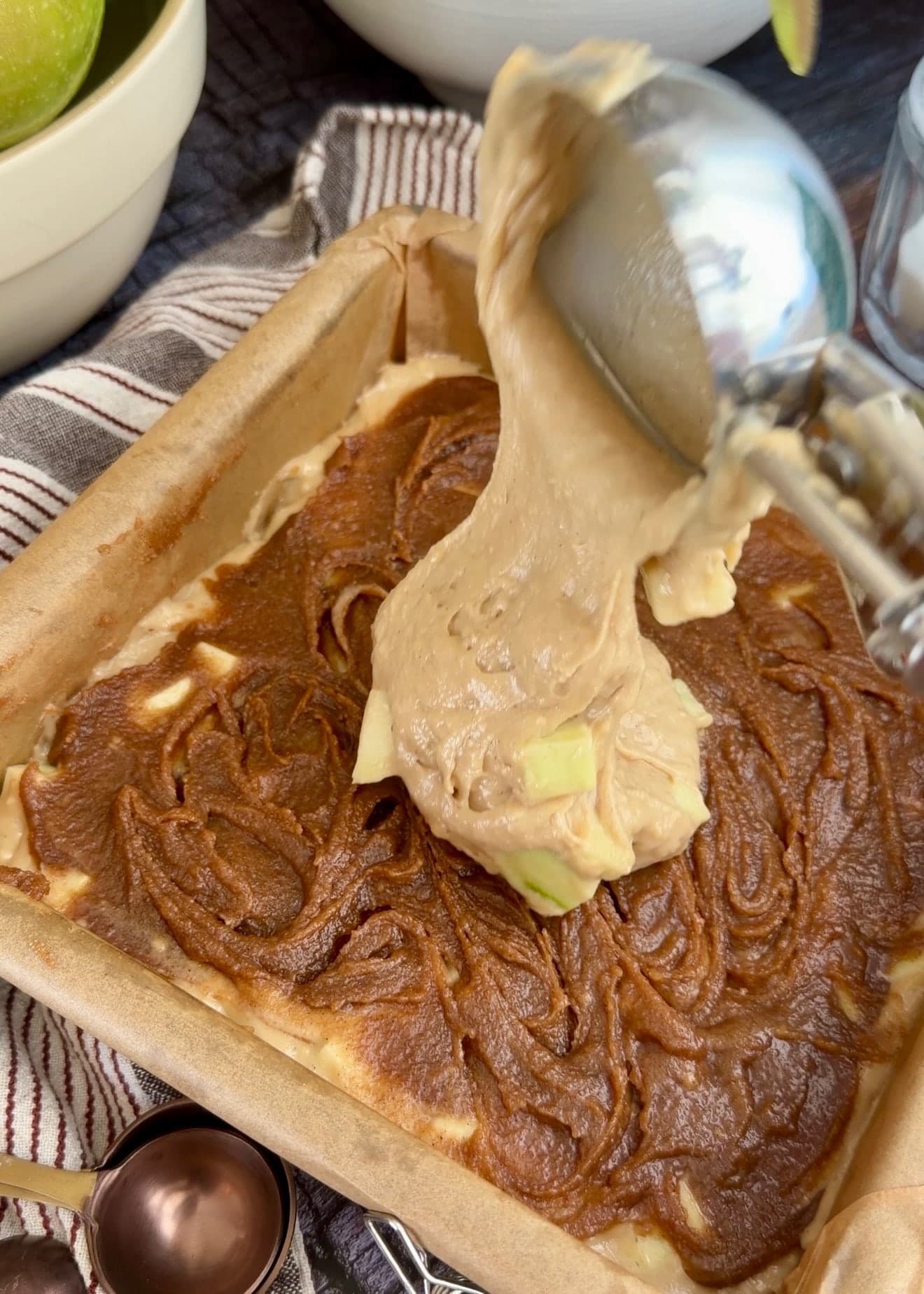 A scoop adding apple batter on top of the cinnamon layer