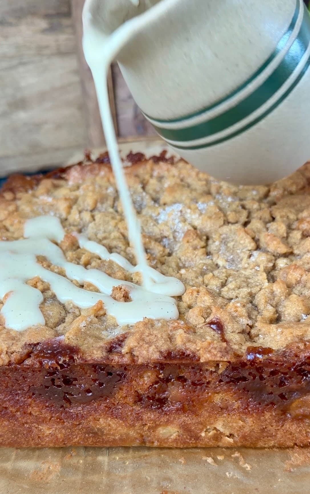 Vanilla glaze pouring onto the crumble from a striped pitcher