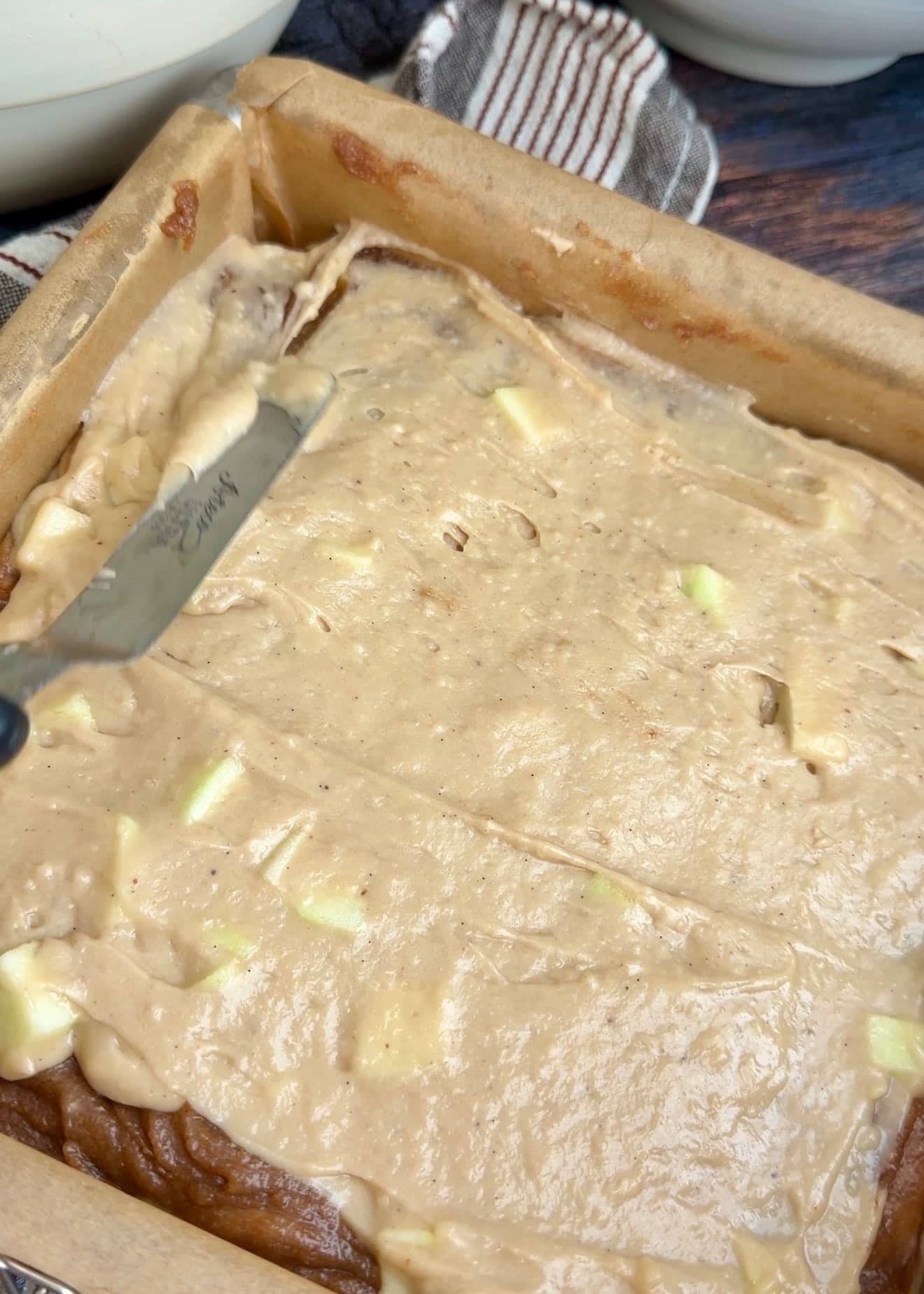 An offset spatula smoothing the upper layer of apple batter