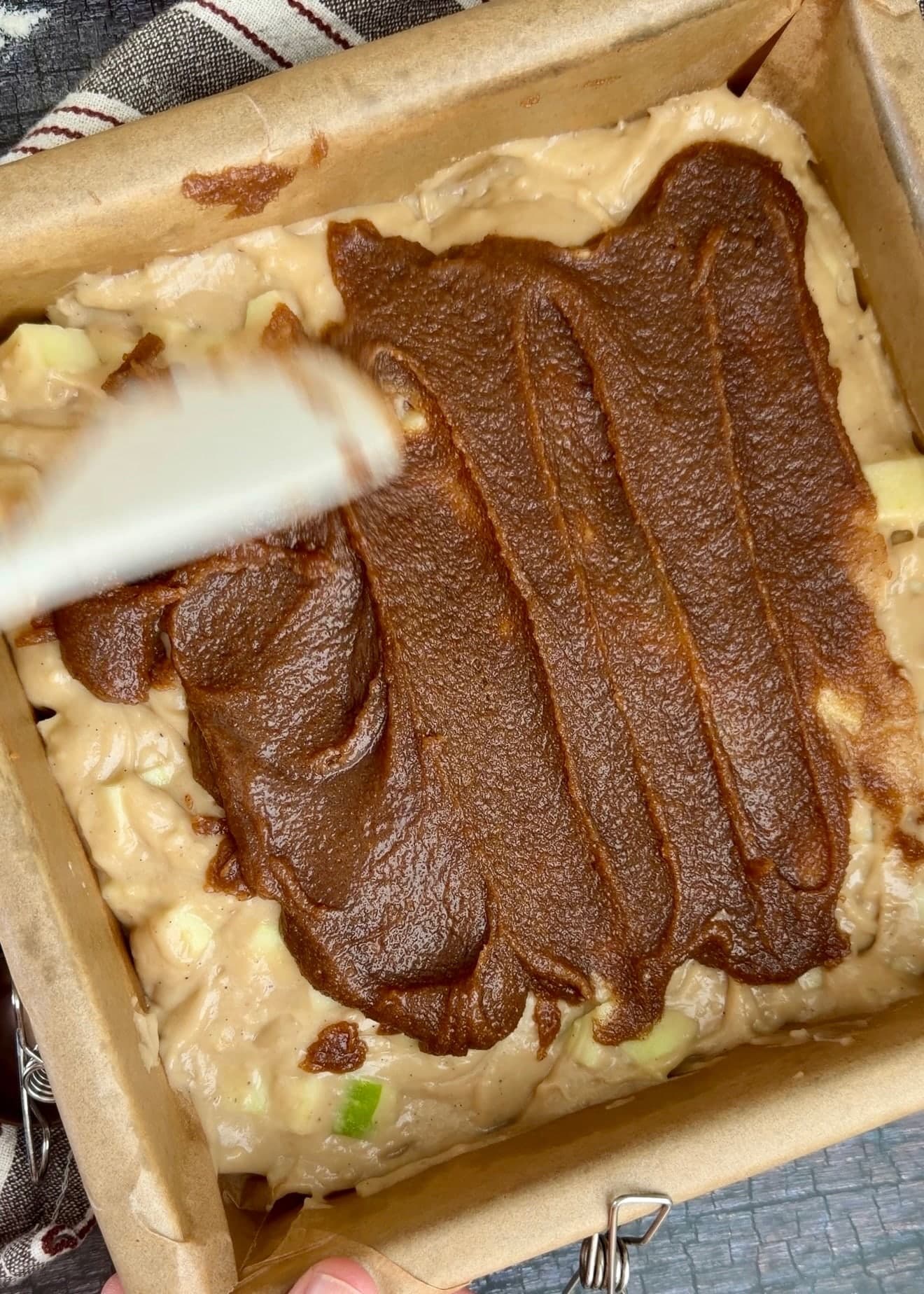 A spatula spreading a brown cinnamon layer over apple cake batter