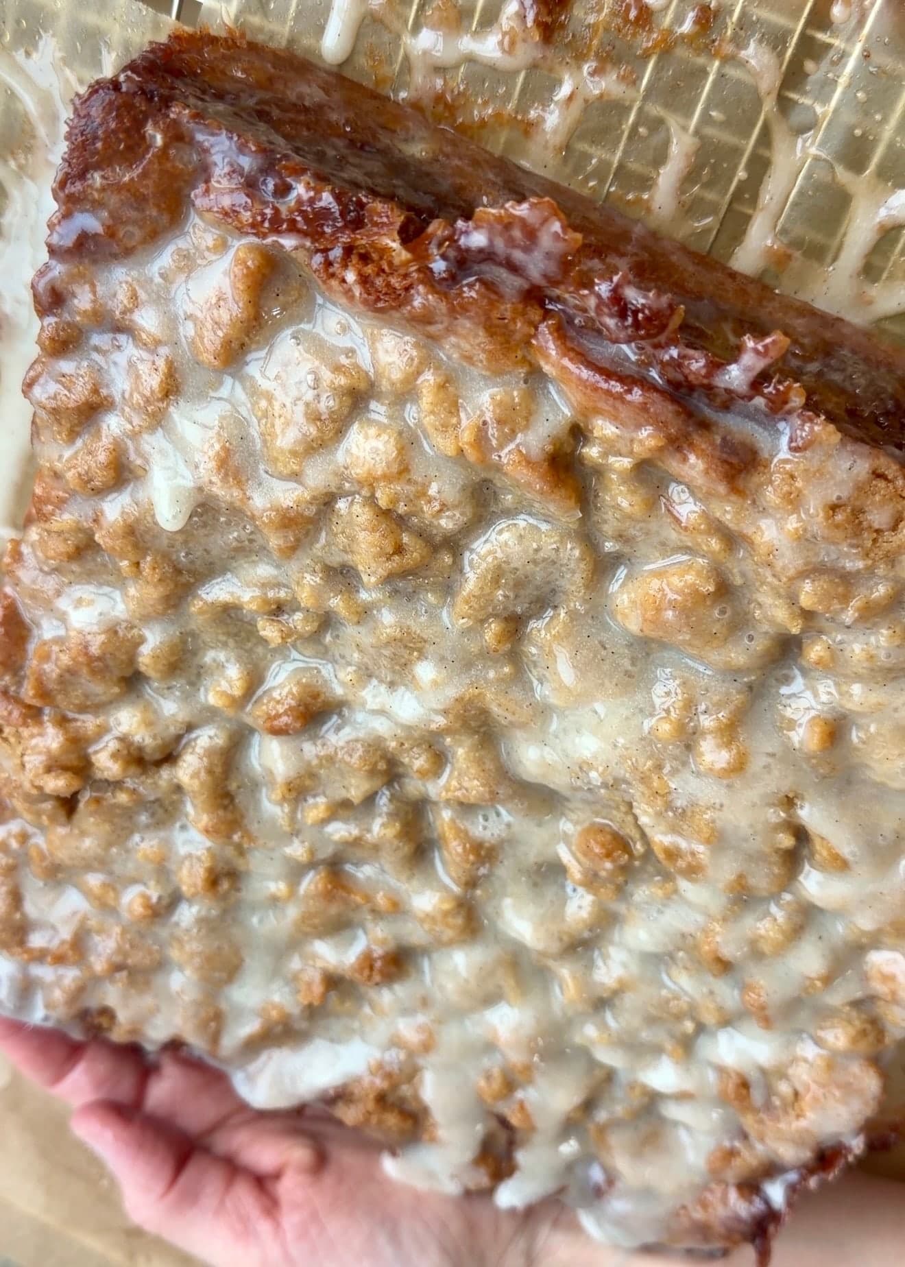 A hand supporting the tilted glazed cake over a rack with glaze drippings below