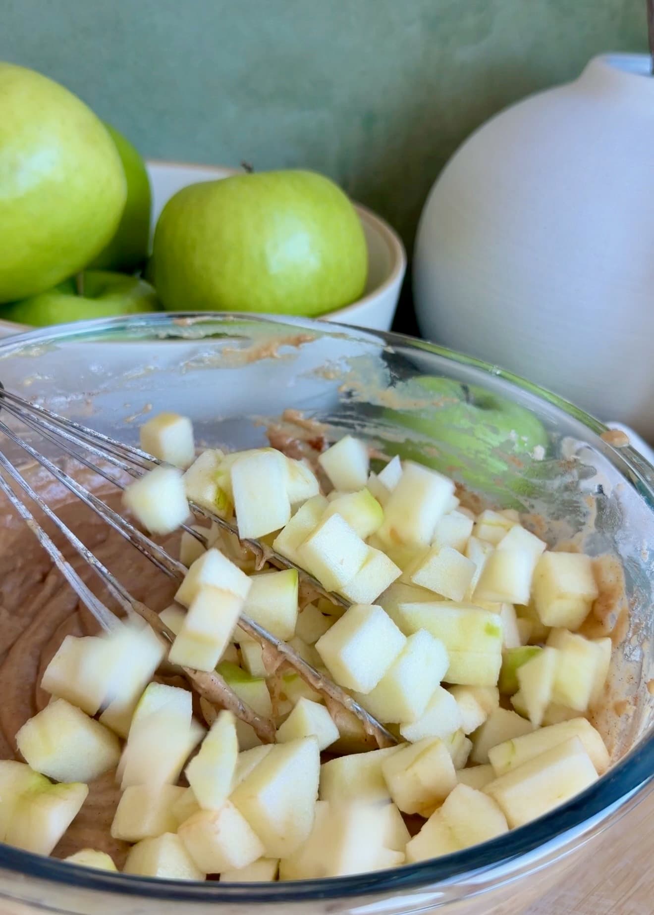 Peeled apple pieces sitting on top of spiced batter in a glass bowl