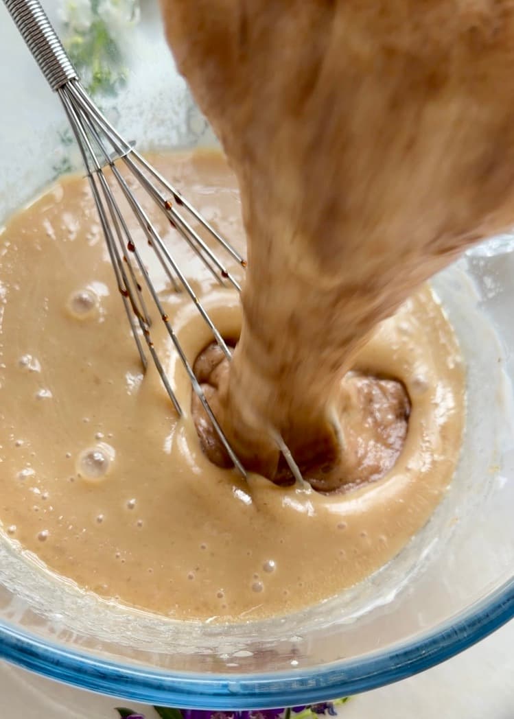 Mashed banana being added to the wet cake mixture