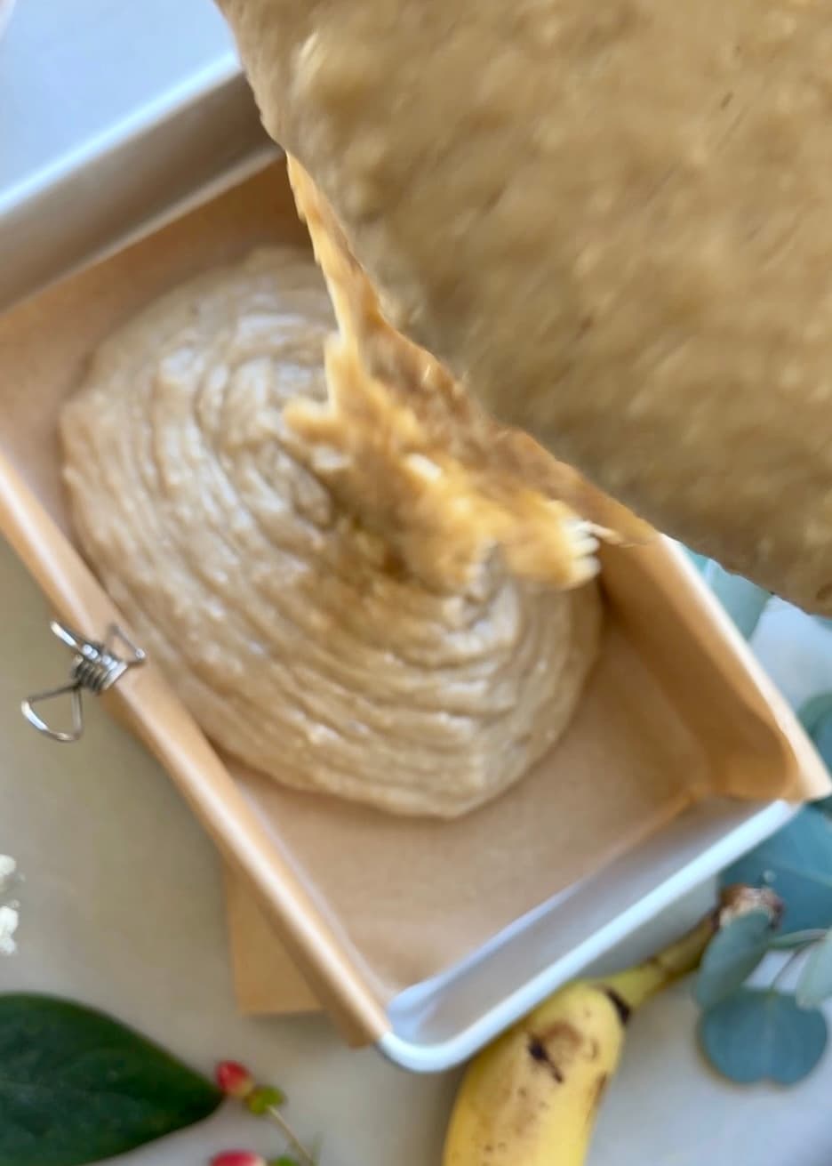 Banana batter being transferred into a lined loaf pan