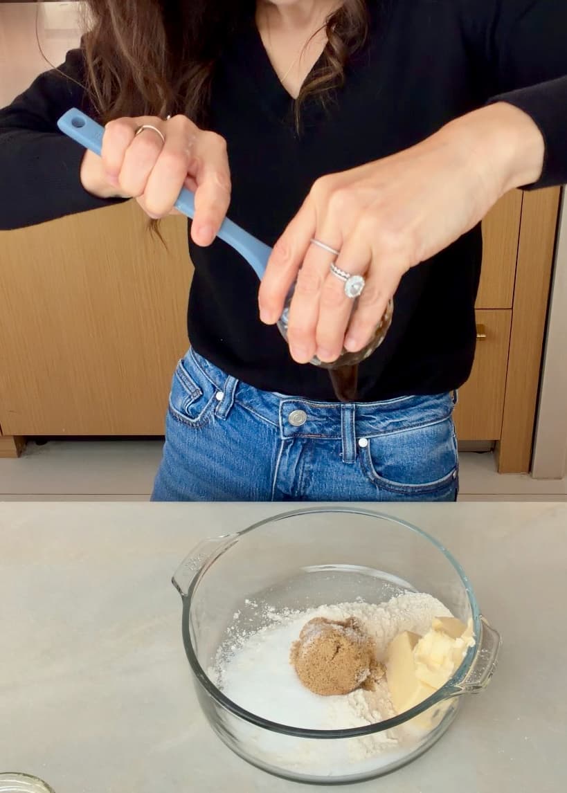 Vanilla bean paste being scraped into a bowl of flour, sugars, and butter