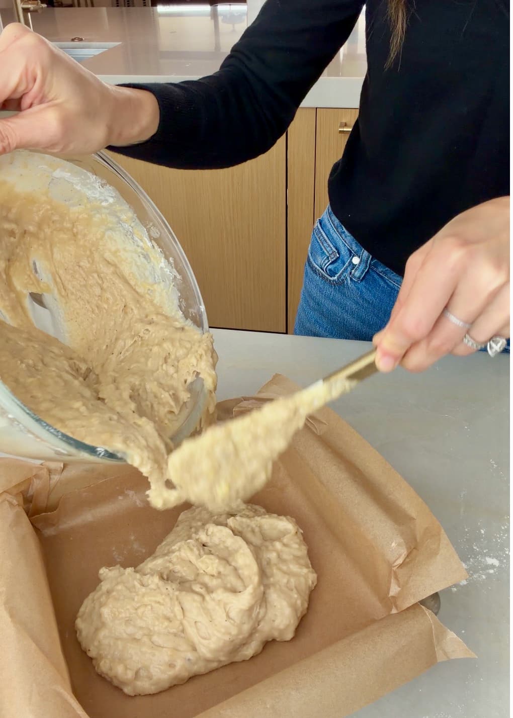 Banana cake batter being scraped into the parchment-lined pan