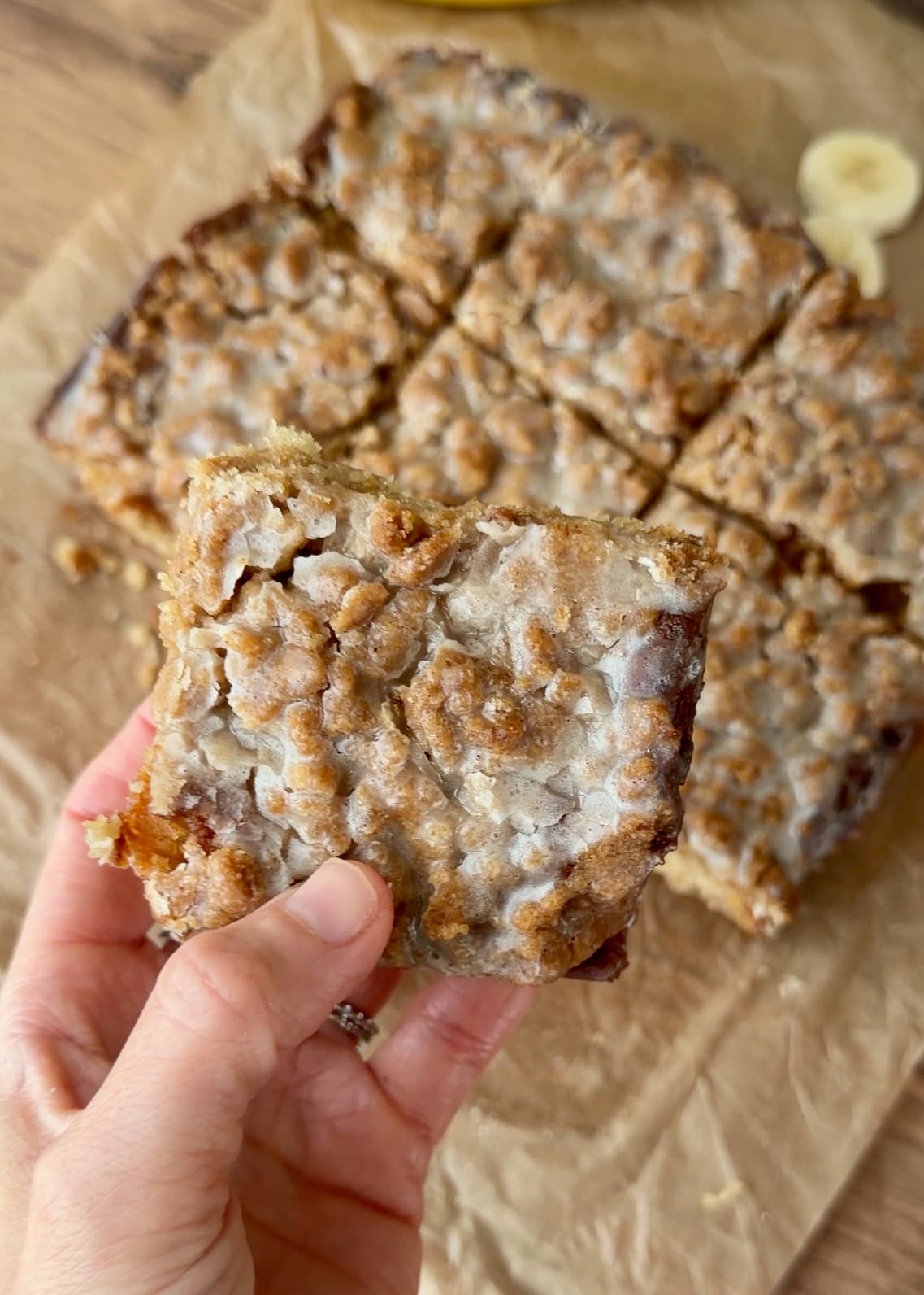 A square of banana coffee cake held up to show its glazed crumble