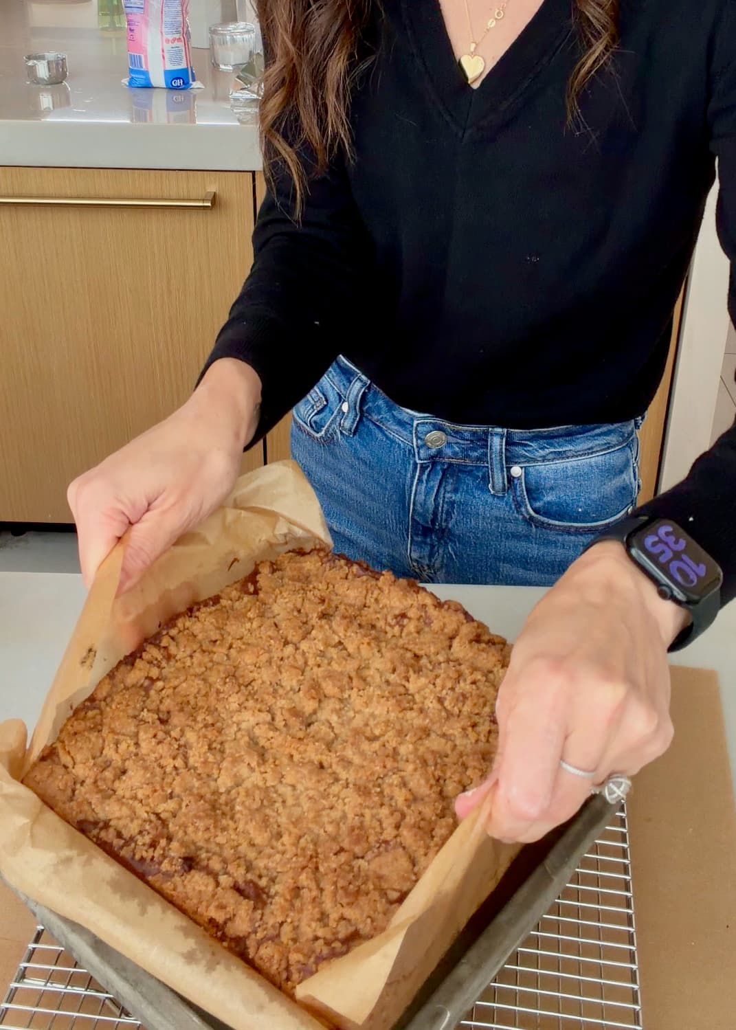 Angela lifting the baked cake from its pan by the parchment handles