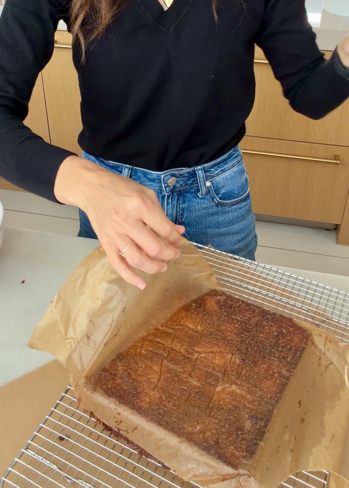 Parchment being peeled from the base of the inverted banana cake on a rack