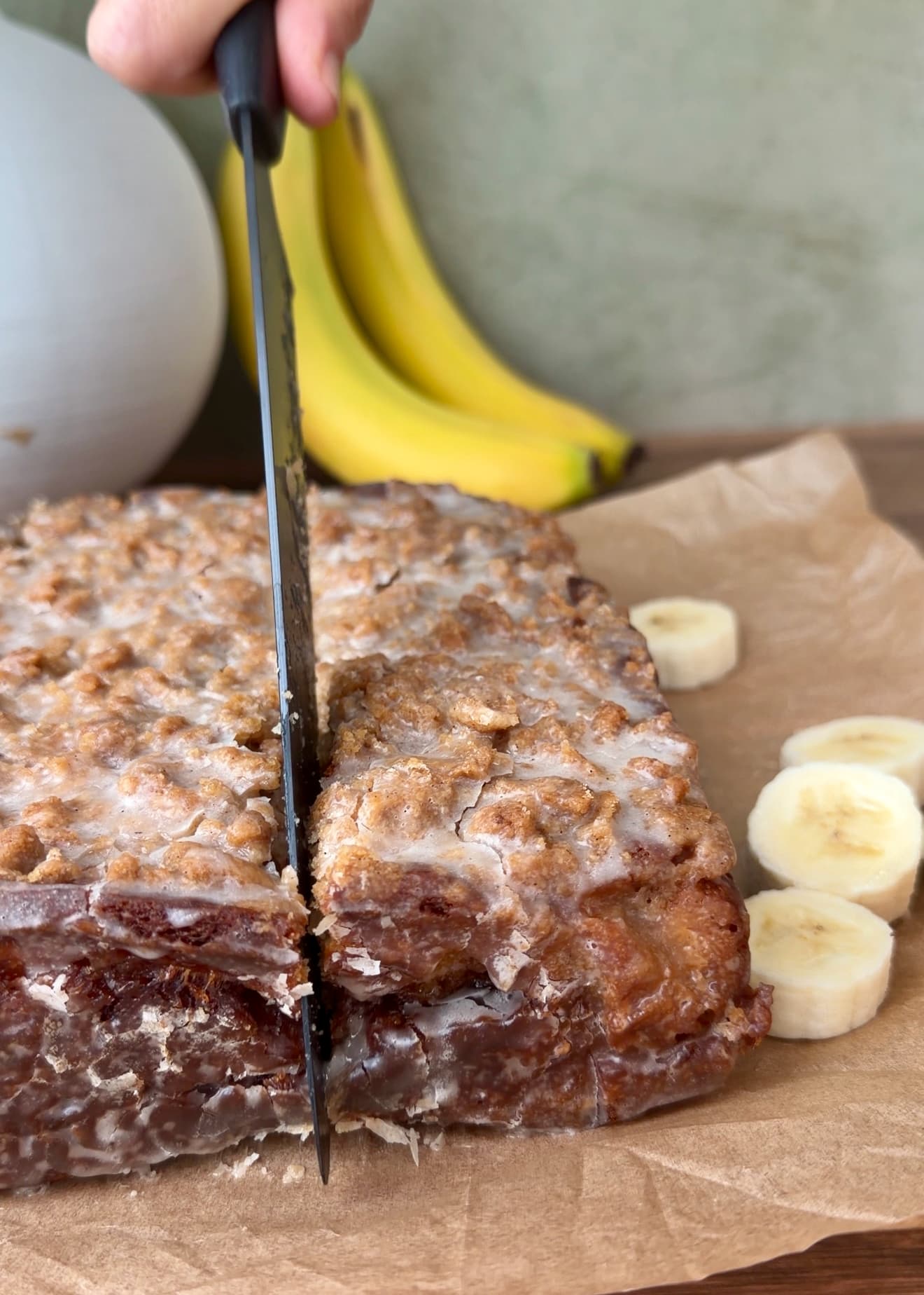 A knife cutting through the glazed banana coffee cake