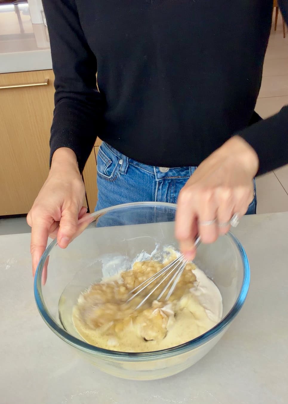 A whisk combining banana with the other wet cake ingredients