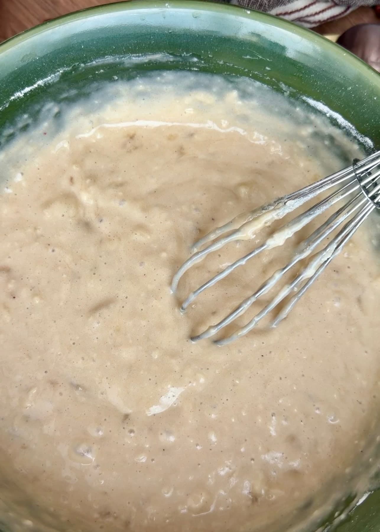 Mixed banana cake batter in a green bowl with a whisk