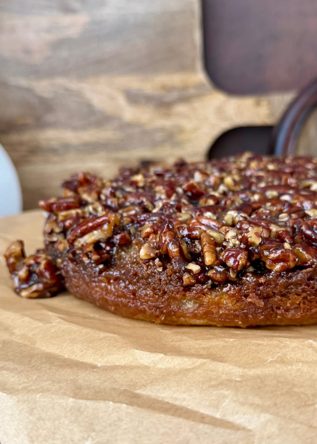 A close side view of banana cake topped with glossy brown sugar pecans
