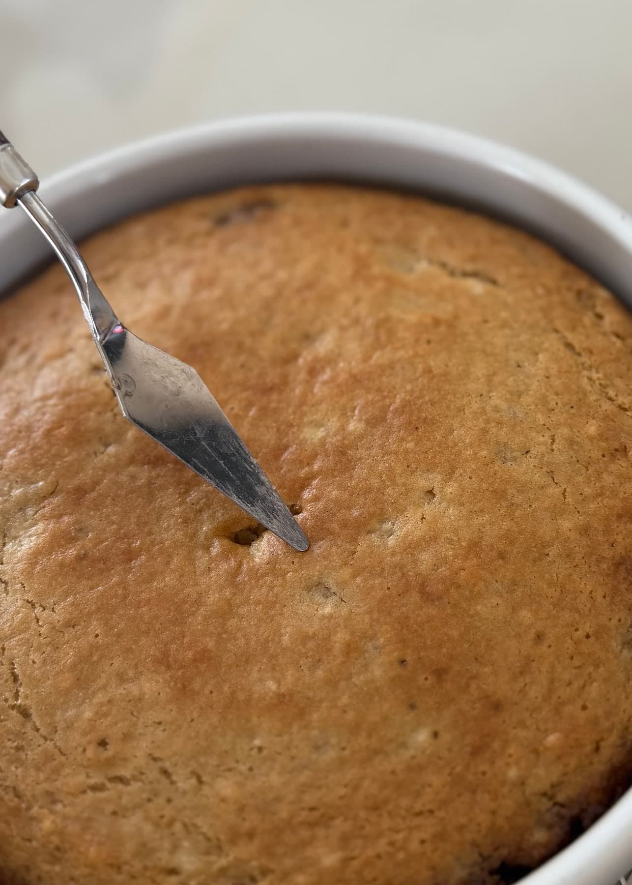 The golden banana cake being checked in the center while still in its pan