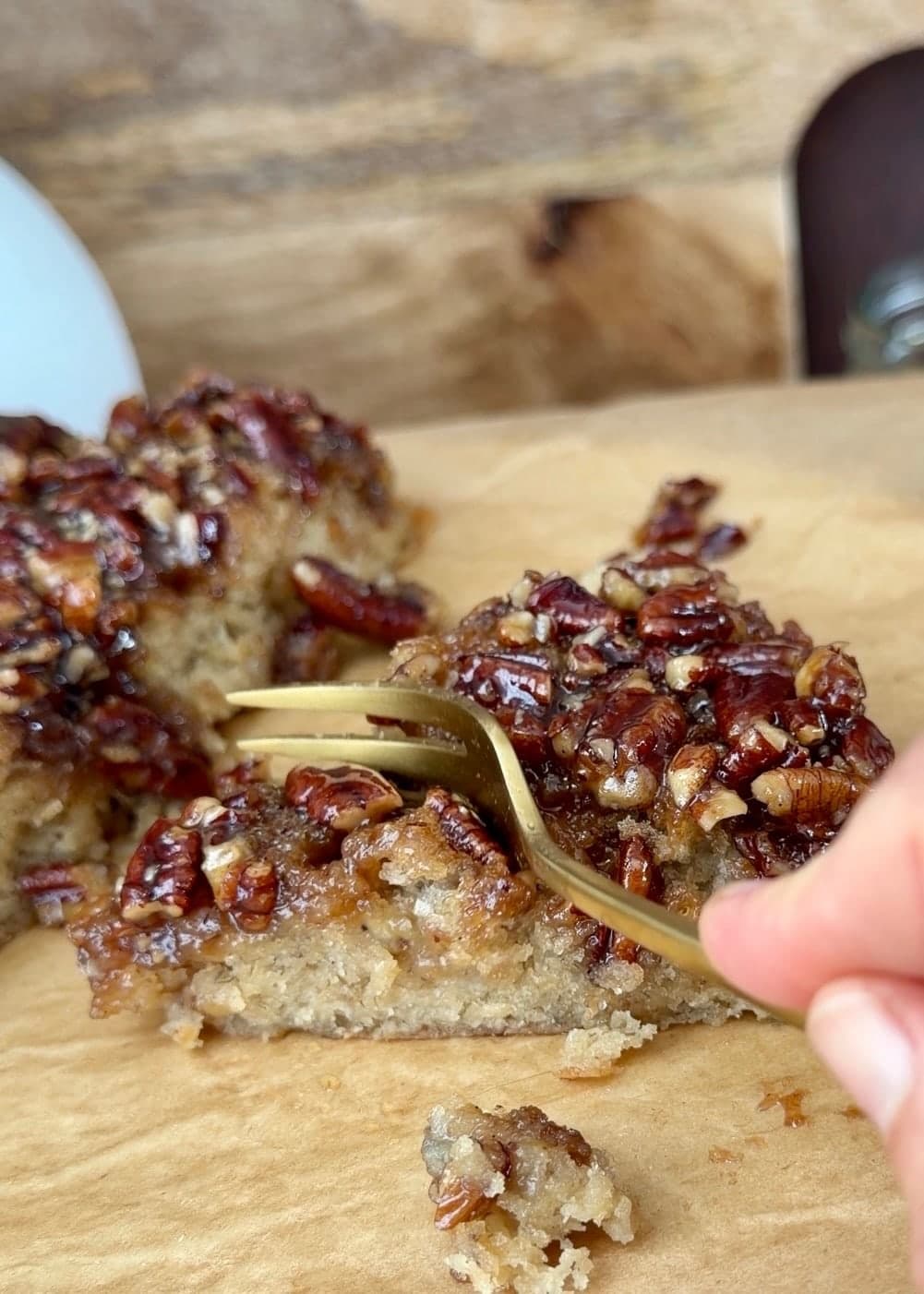A fork cutting into a slice of banana cake with sticky pecans