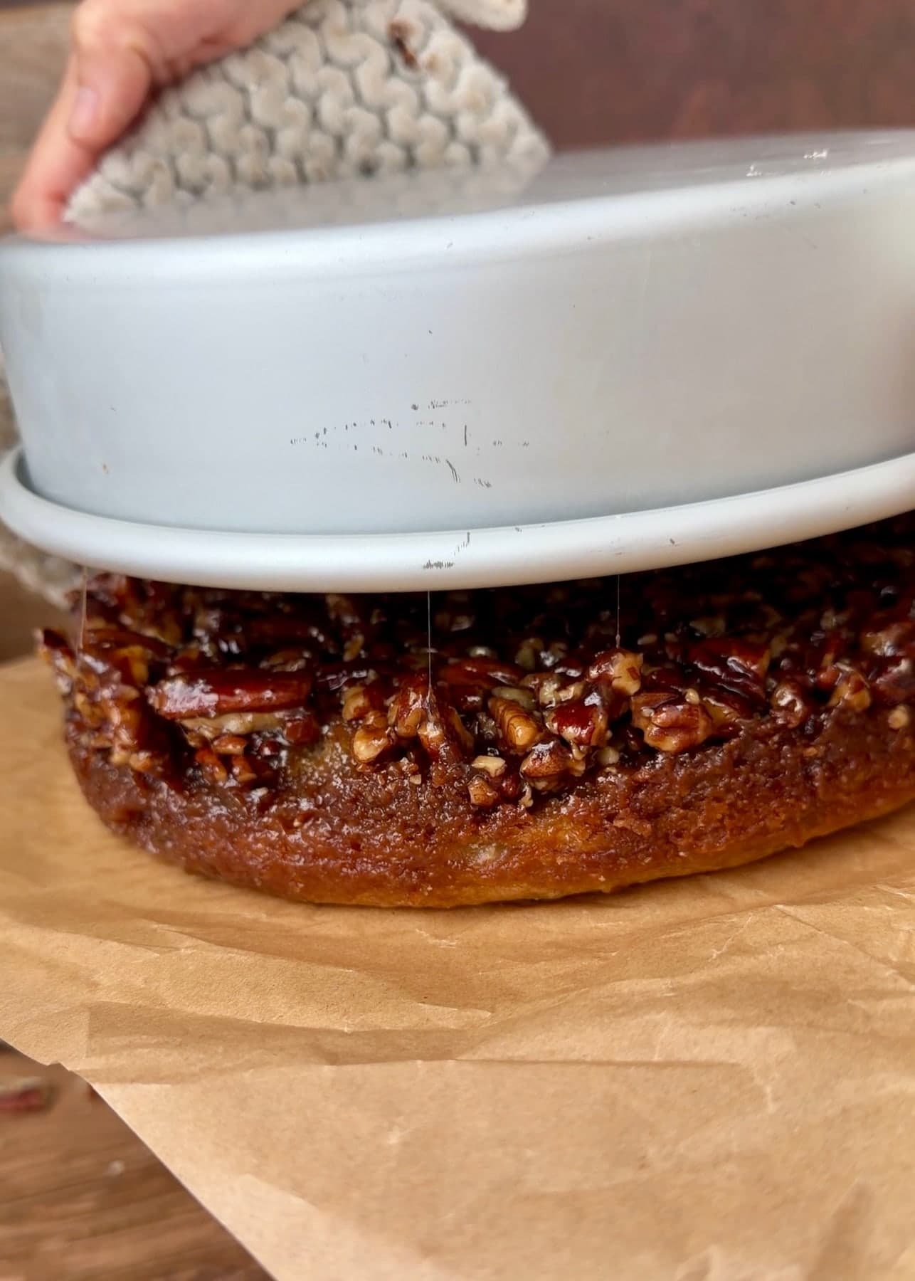 The inverted pan being lifted away to reveal the sticky pecan topping