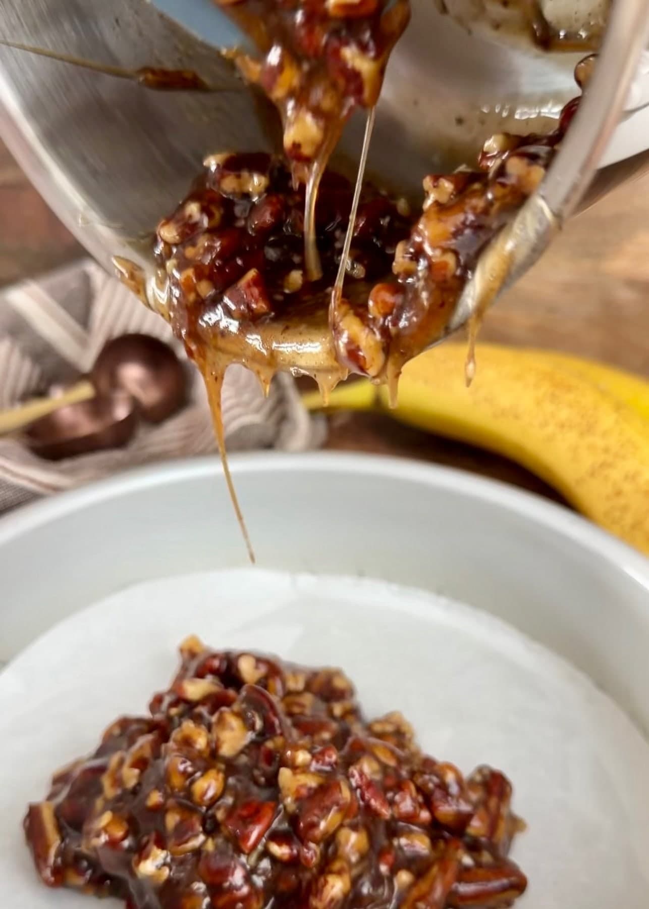 Pecan topping being poured into a parchment-lined round cake pan