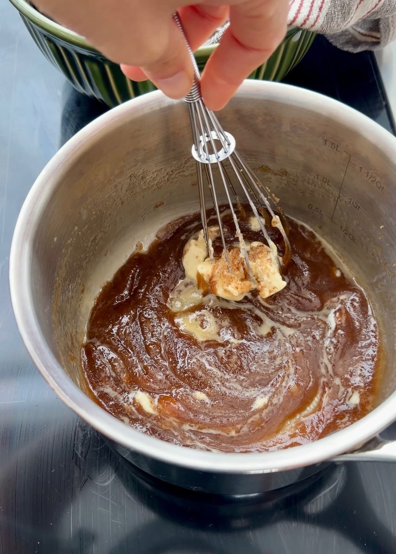 A whisk stirring partially melted butter into brown sugar in a saucepan