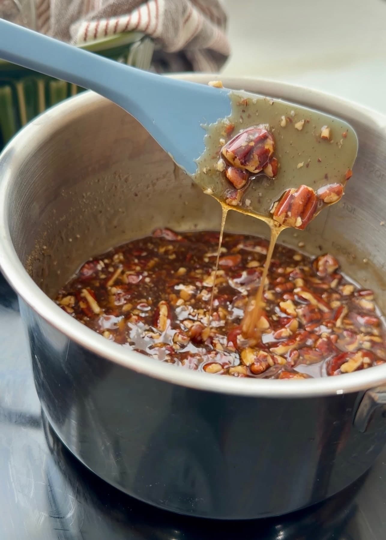 Glossy pecan topping dripping from a blue spatula into the saucepan
