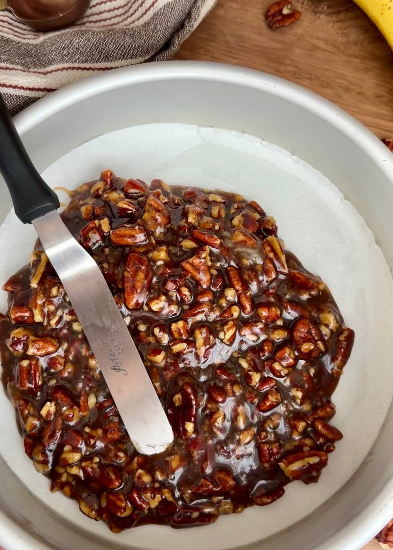An offset spatula spreading pecans and brown sugar topping in the pan