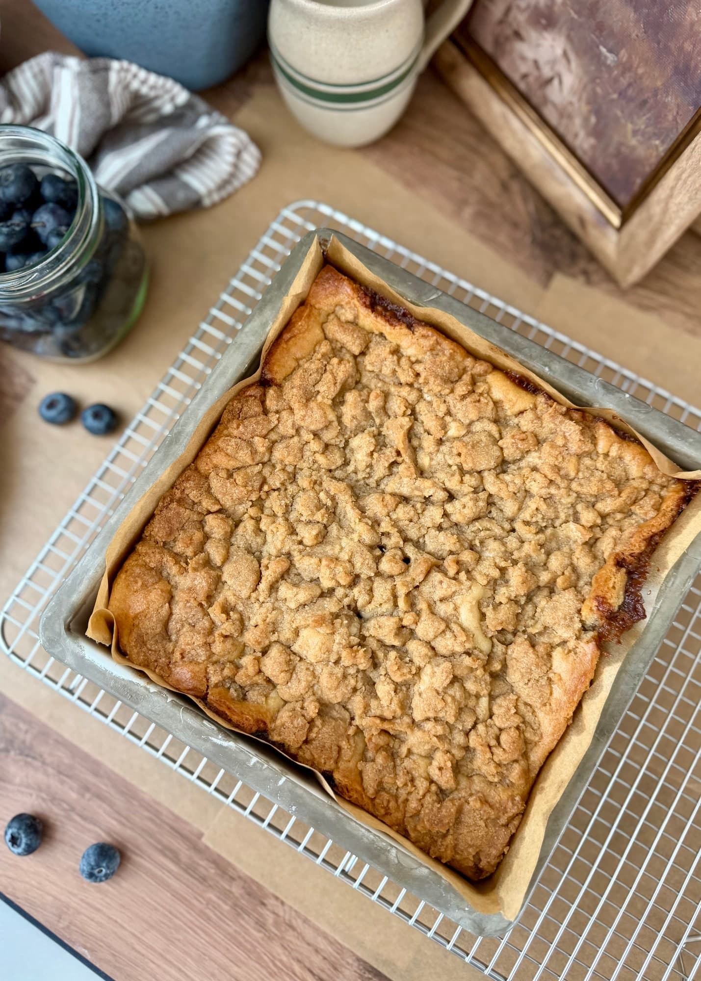 Golden crumble-topped blueberry cake resting in its parchment-lined pan