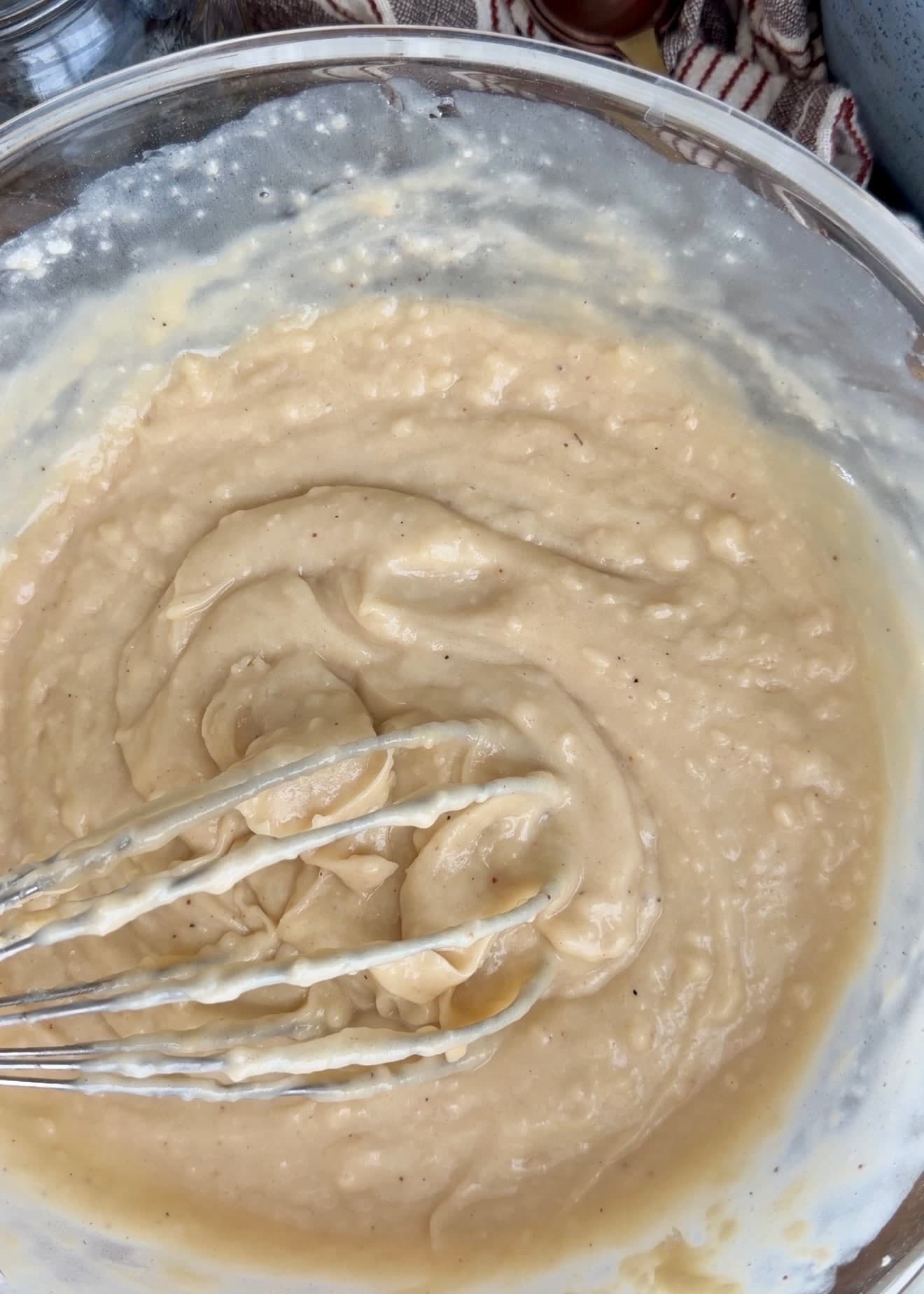 Thick pale cake batter holding whisk trails in a glass bowl