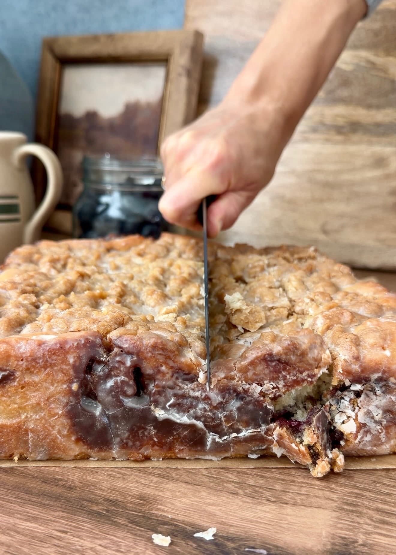 A knife cutting through the set glaze and blueberry cake