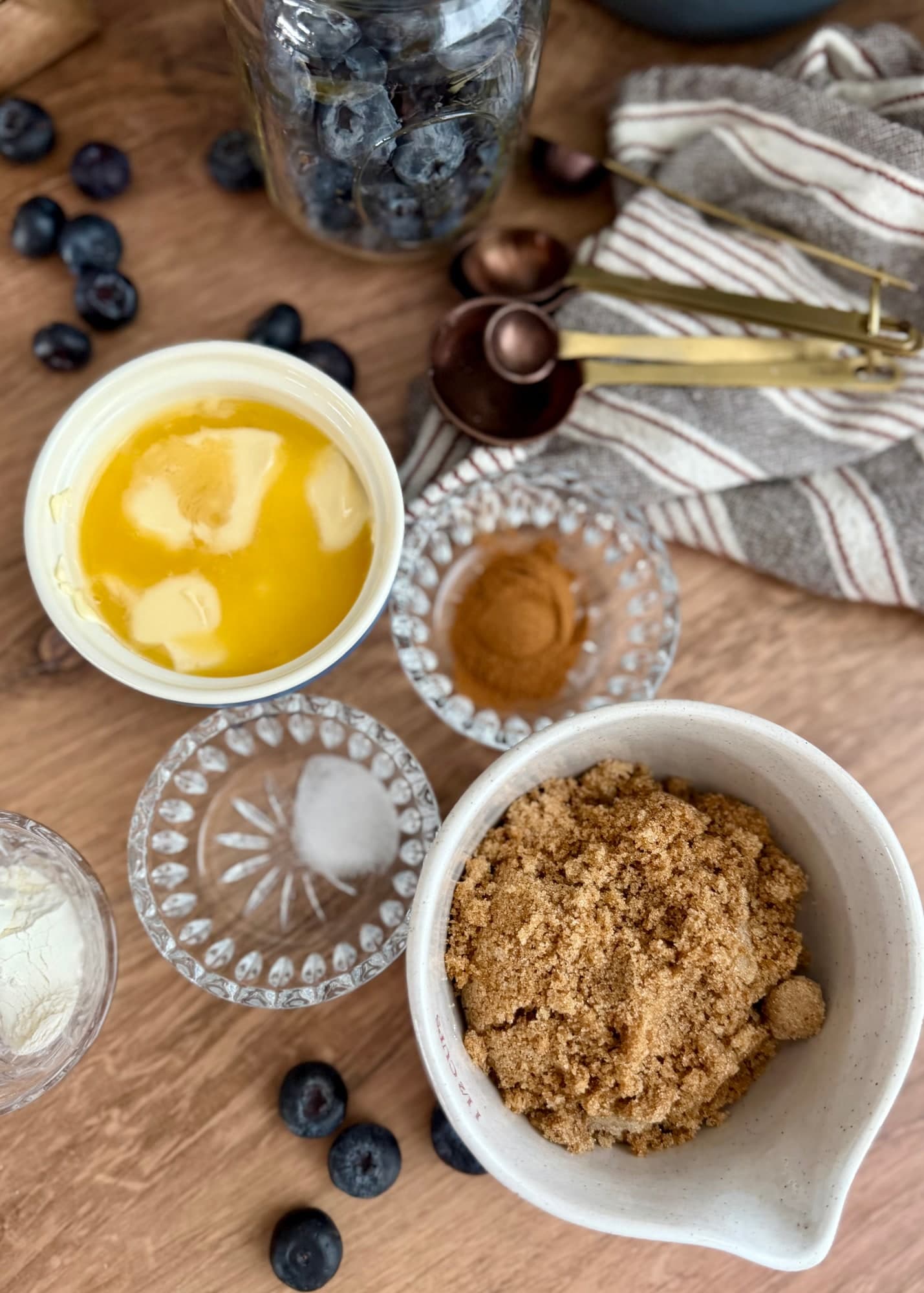 Brown sugar, butter, cinnamon, flour, and salt arranged beside a jar of blueberries