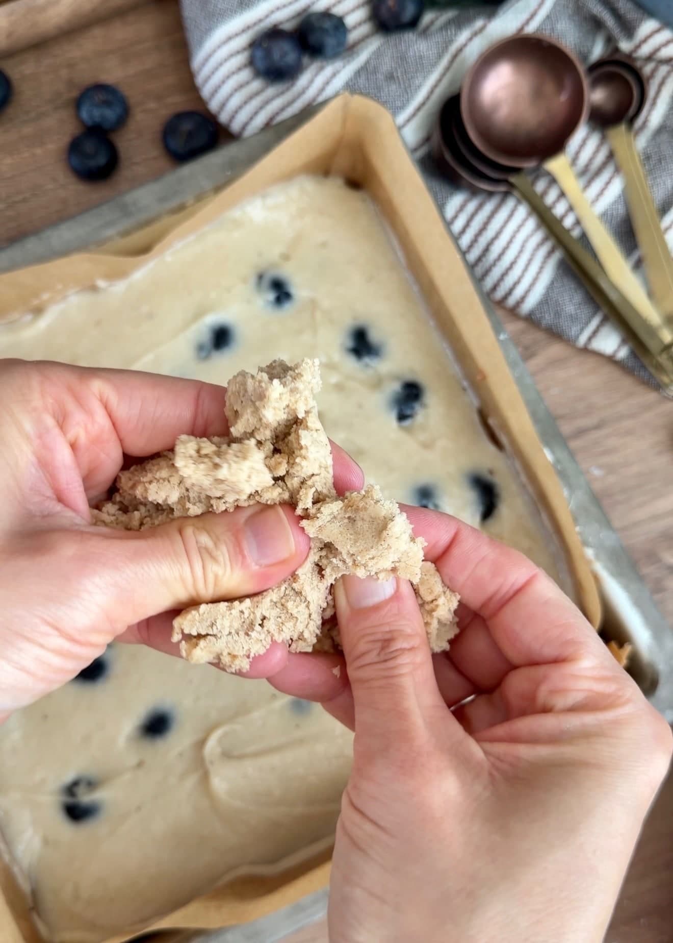 Hands breaking chilled crumble into large pieces above the cake