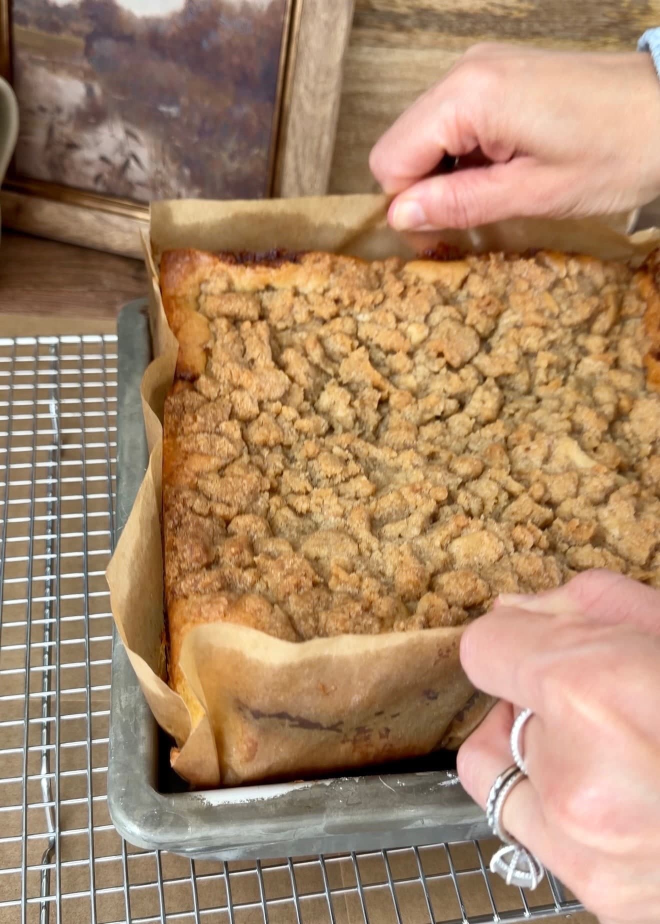 Hands holding the parchment overhangs to lift the baked cake from its pan