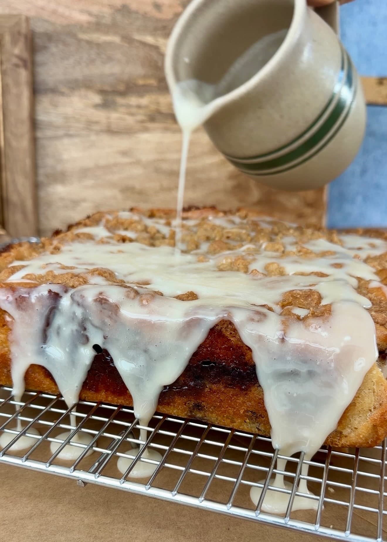 Thin vanilla glaze running over the crumble and caramelized sides of the blueberry cake