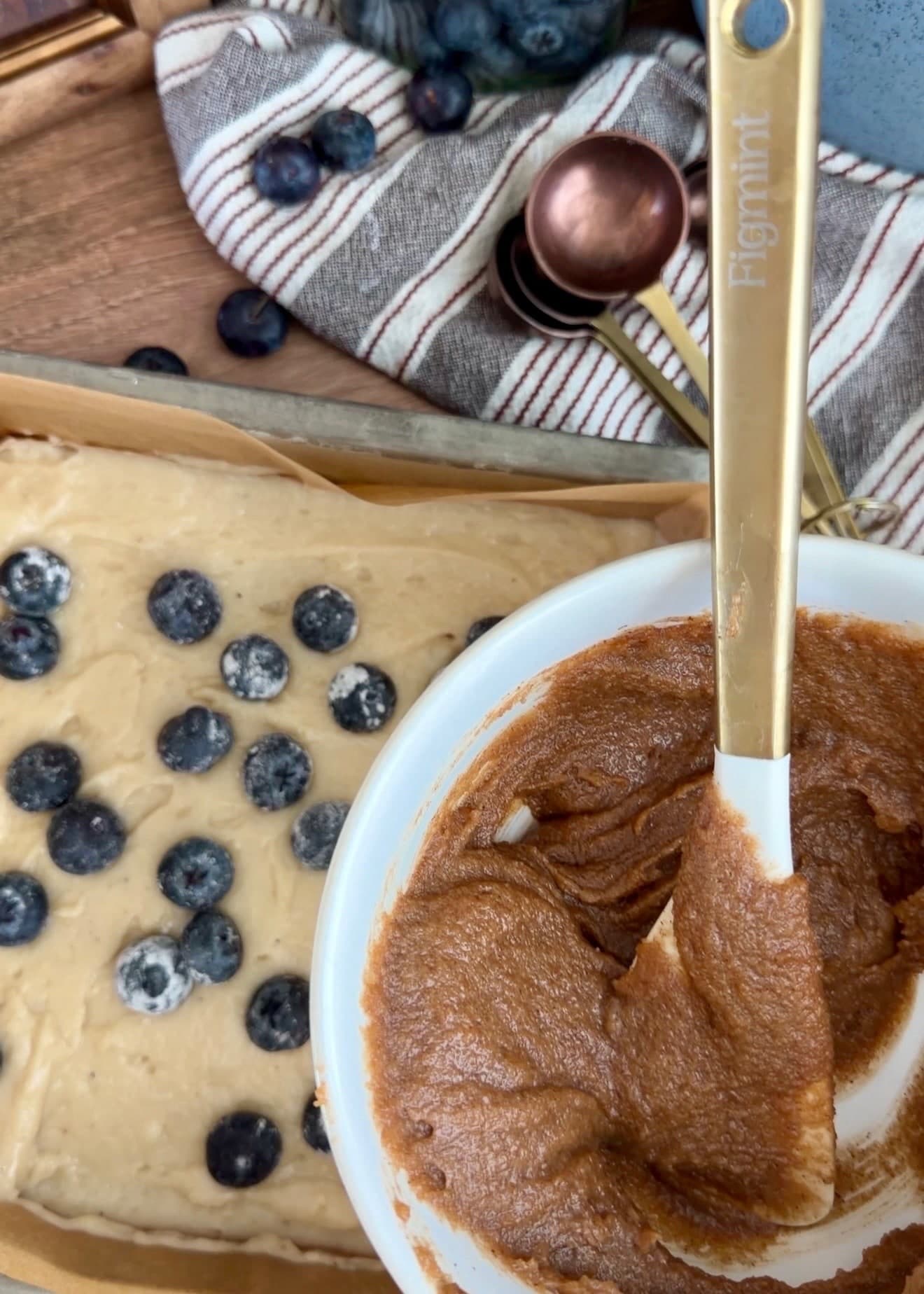 A bowl of thick cinnamon filling beside the first layer of batter and blueberries