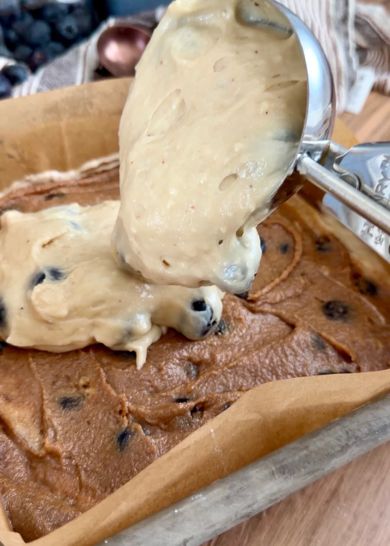 A scoop dropping blueberry batter over the cinnamon filling