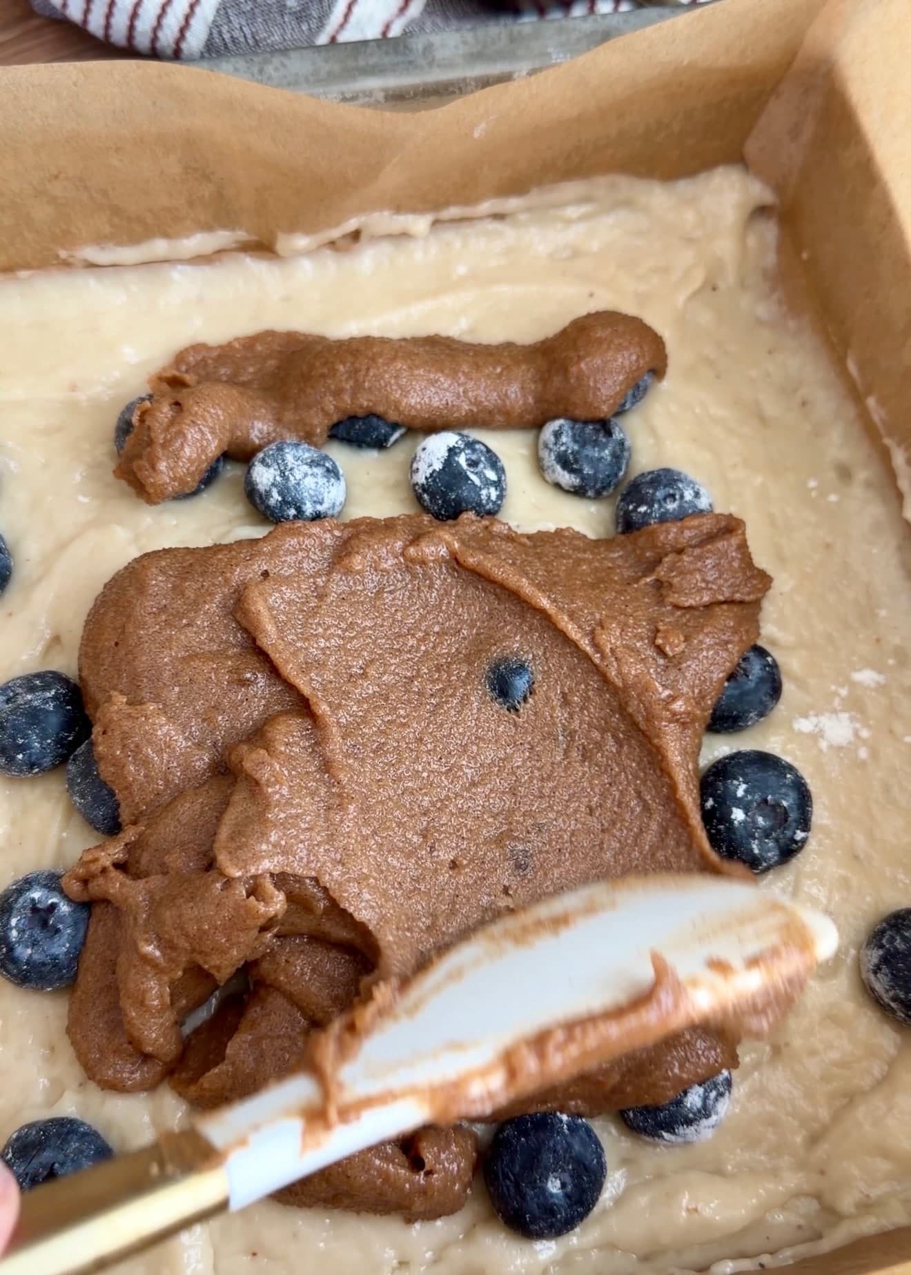 A spatula spreading thick cinnamon filling over blueberries and batter