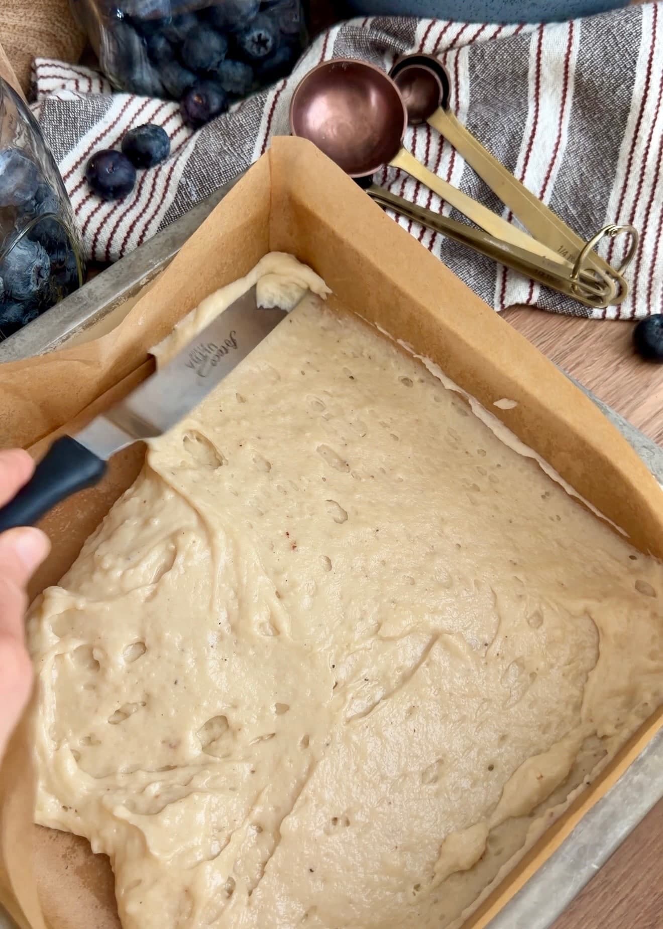 An offset spatula spreading batter into a parchment-lined square pan
