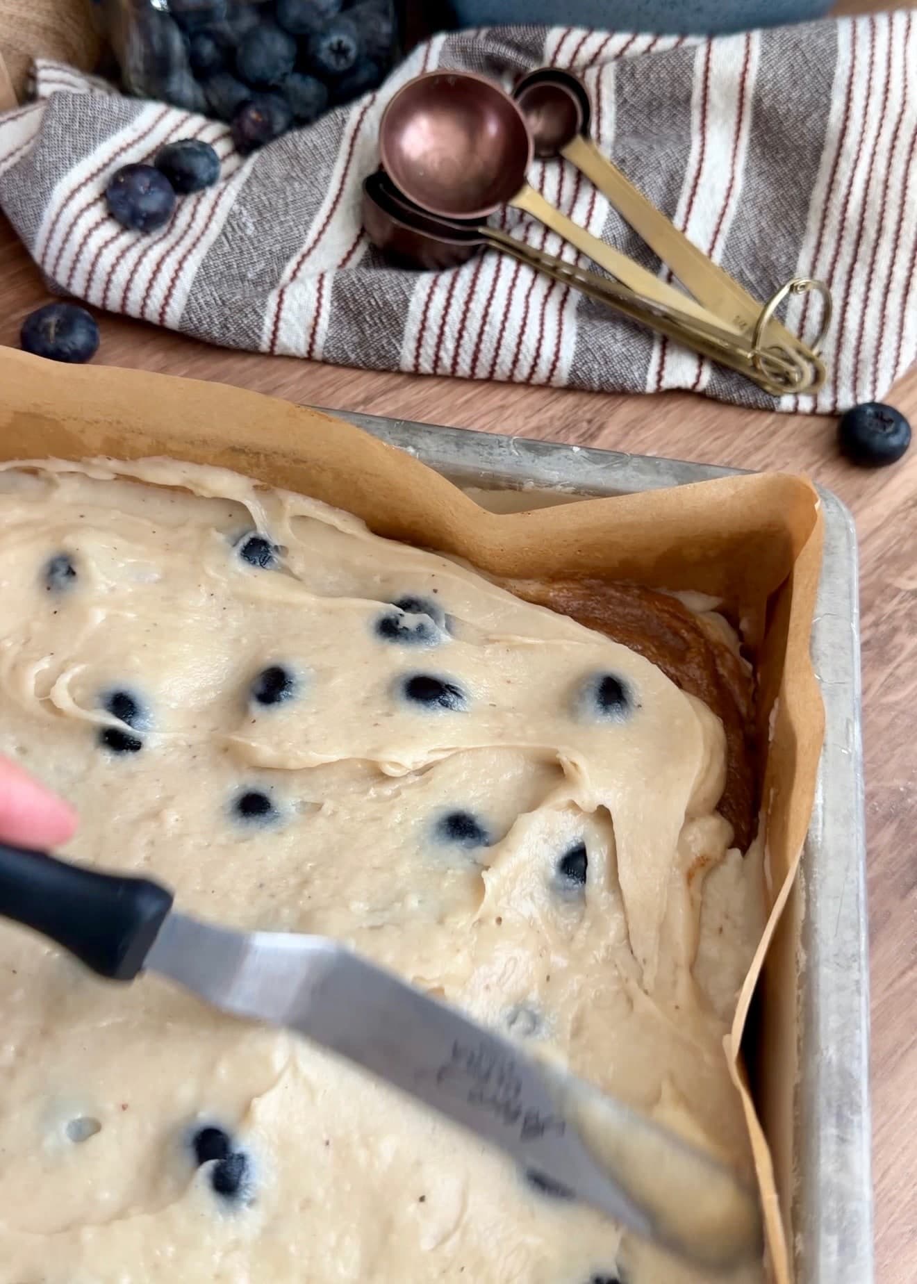 An offset spatula smoothing the top layer of blueberry batter