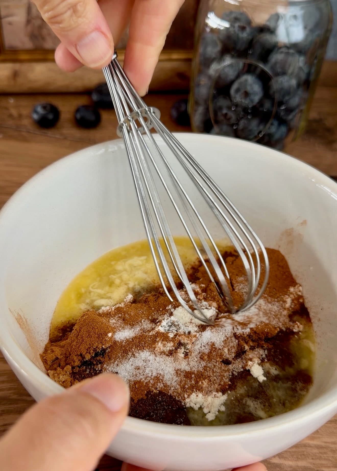 A whisk combining melted butter, cinnamon, sugar, and flour in a white bowl