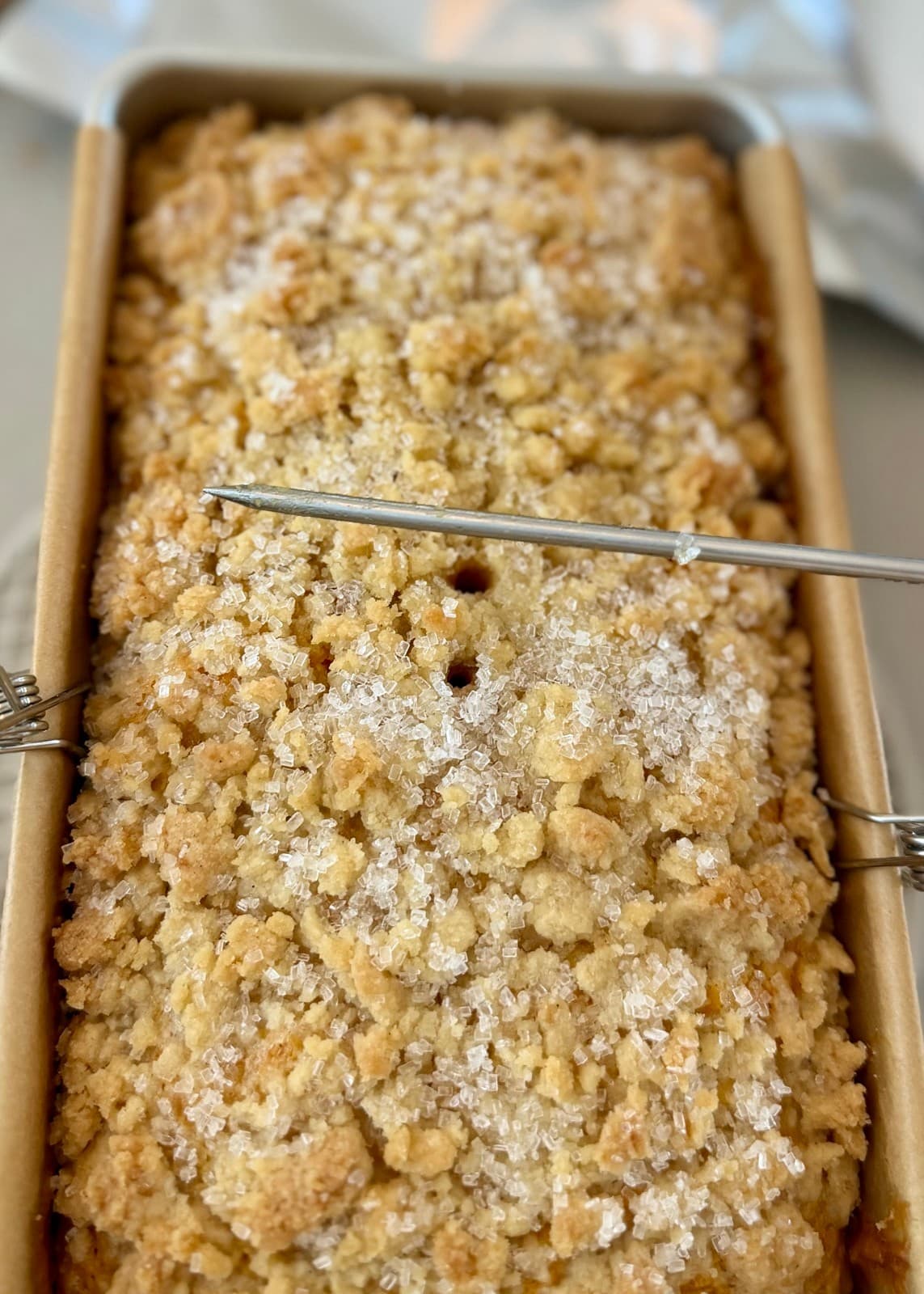 A metal tester held above the baked loaf with small crumbs attached