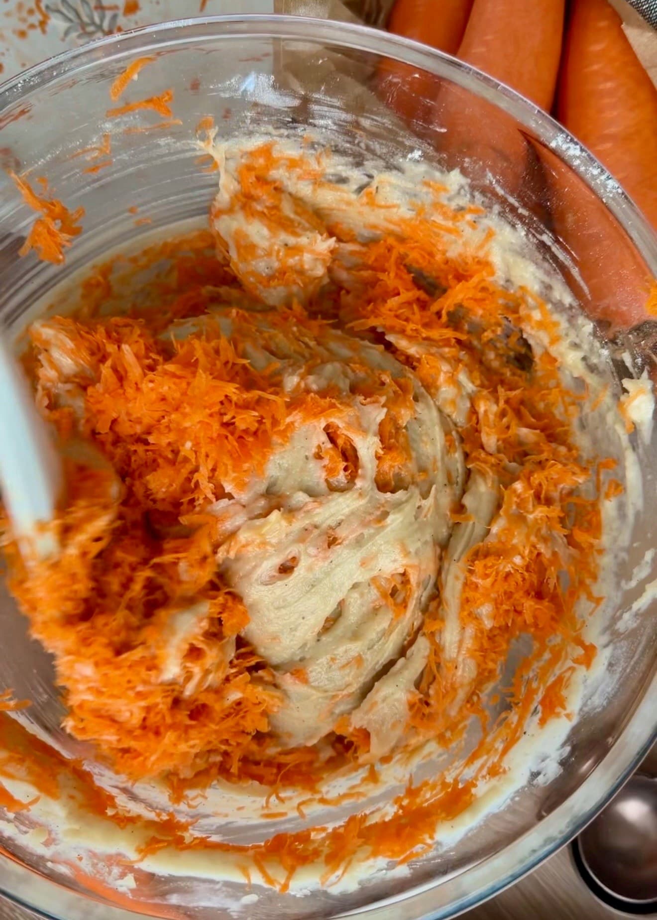 A spatula folding grated carrots through the batter