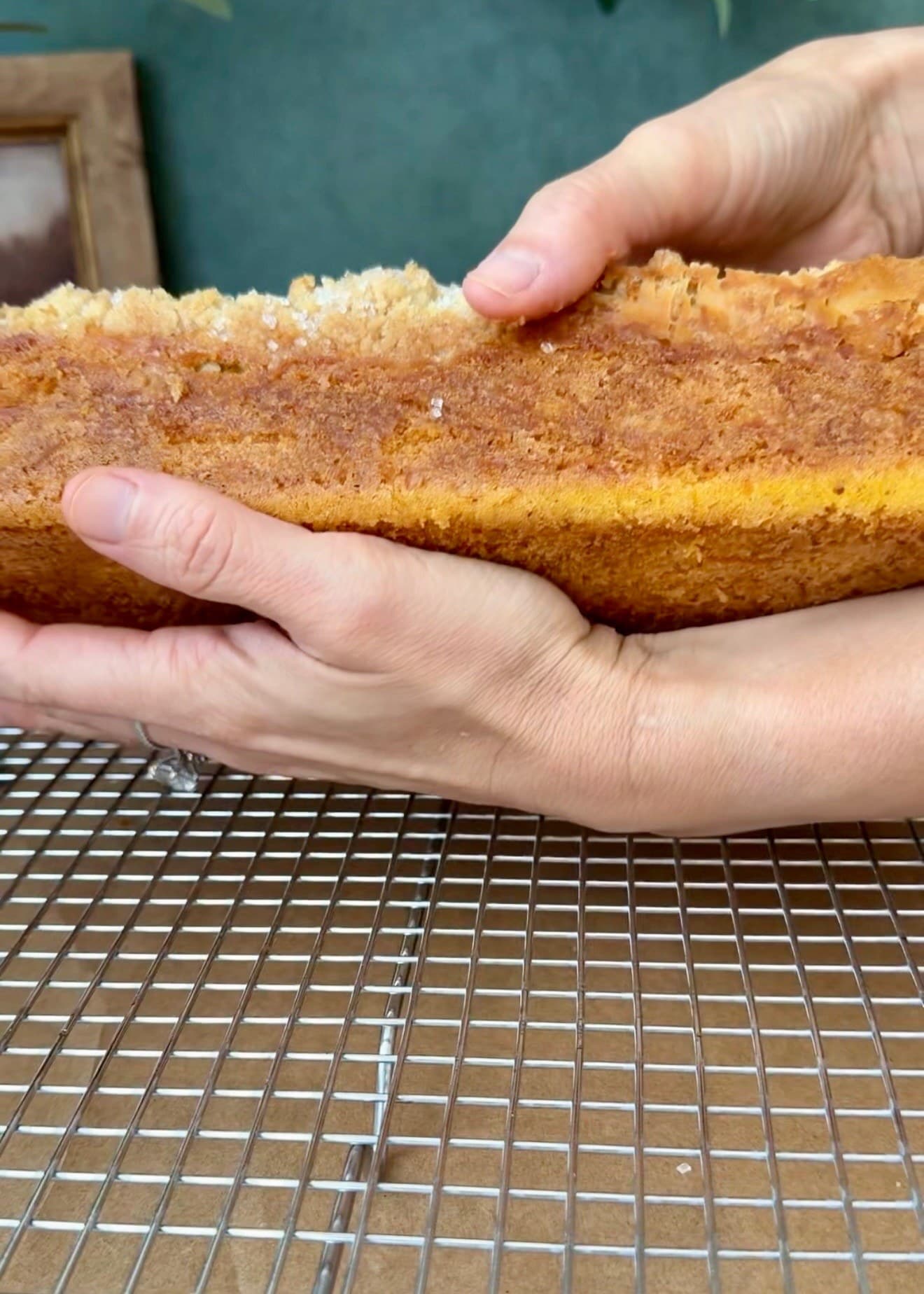 Both hands supporting the unglazed loaf on its side above a wire rack, with the bare base exposed