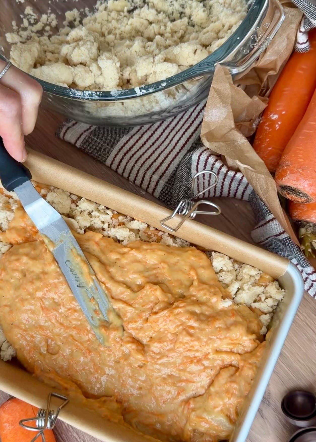 An offset spatula spreading carrot batter over streusel