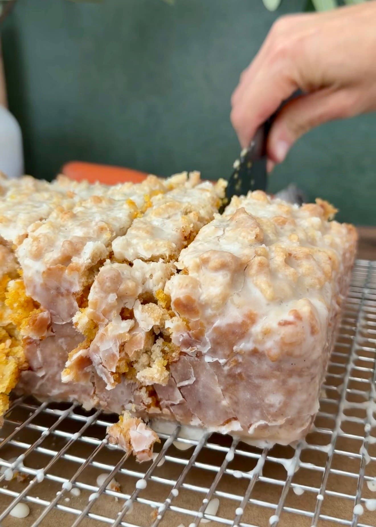 A knife slicing the glazed carrot loaf on a rack