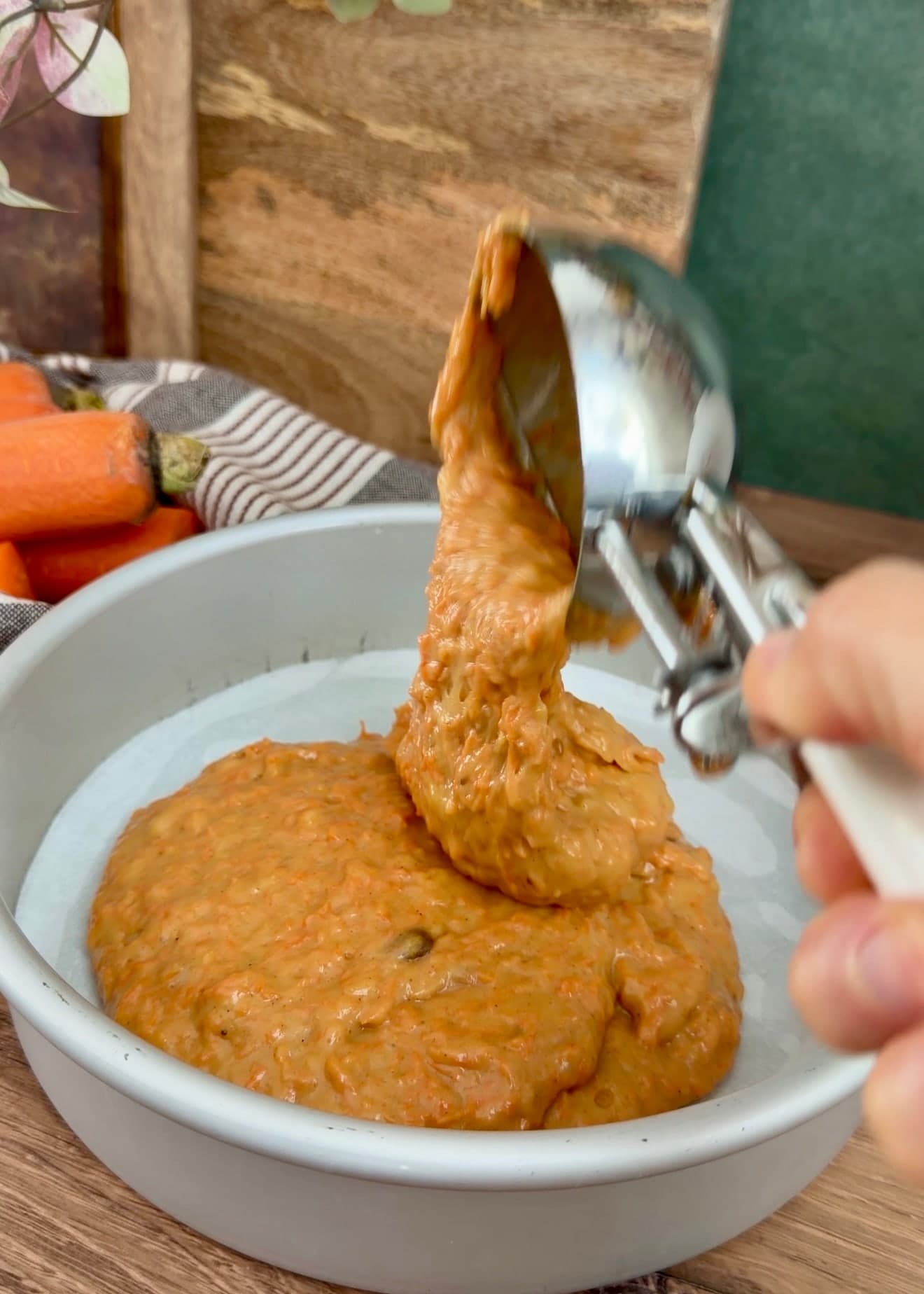 Carrot cake batter scooped into a parchment-lined round cake pan