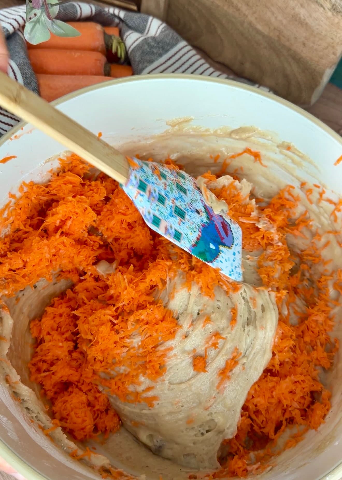 Finely grated carrots being folded gently into the cake batter
