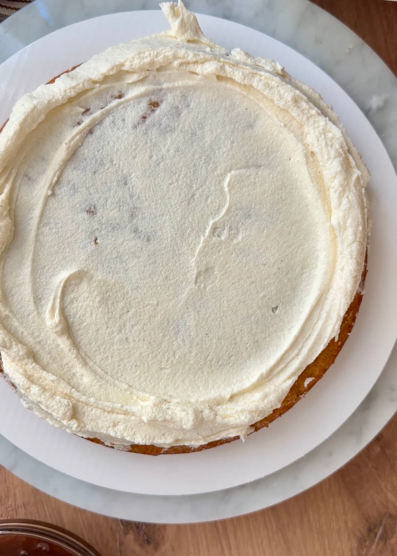 Frosting spread over carrot cake with a raised border around the edge