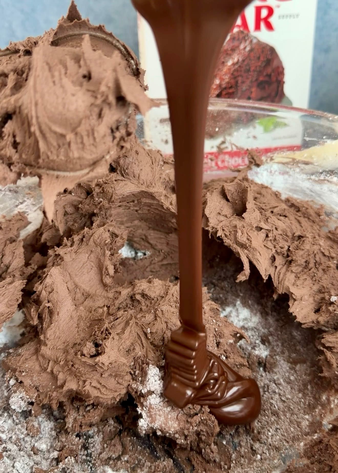 A ribbon of melted chocolate pouring into the chocolate buttercream base