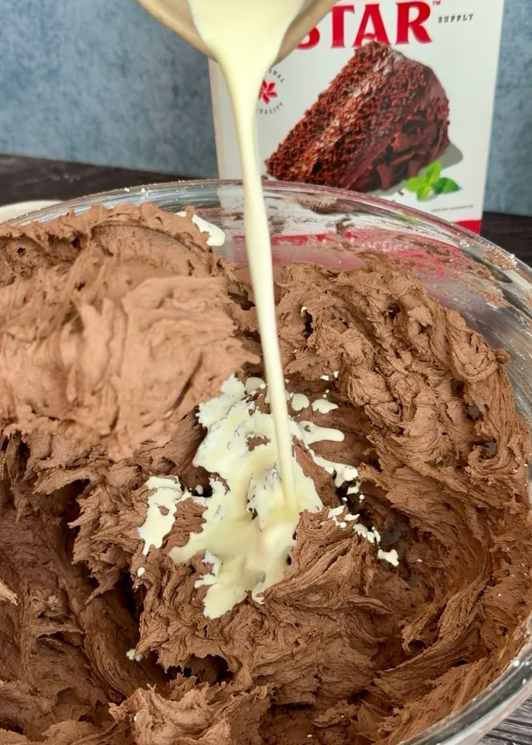 Cream pouring into chocolate buttercream in a glass bowl