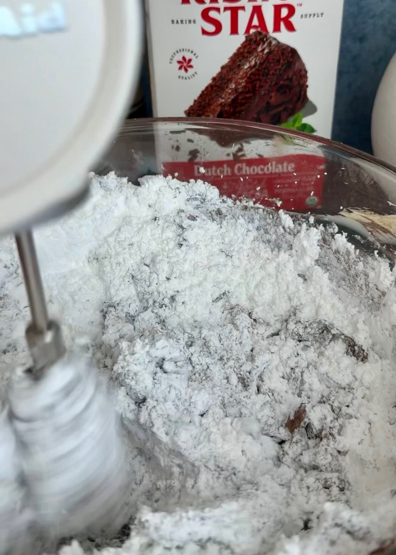 Powdered sugar over the cocoa and butter mixture beside the hand-mixer beaters
